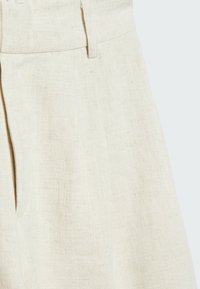 Shorts en lin de couleur beige clair, avec un devant plat, des plis latéraux et une texture lisse. La ceinture comporte des passants pour y ajouter une ceinture.