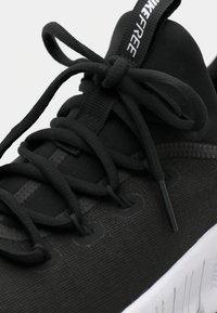 Scarpa atletica nera con tomaia in mesh testurizzato, lacci piatti e suola bianca con dettagli scanalati. Il logo è visibile sulla linguetta.