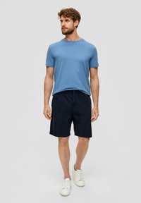 Hellblaues Baumwoll-T-Shirt, Rundhalsausschnitt, kombiniert mit dunkelblauen Shorts, elastischem Bund und weißen Turnschuhen. Einfaches, lässiges Design.