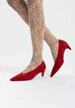 Cizme roșii din suede cu vârful ascuțit și toc kitten mic, asortate cu ciorapi bej din plasă cu un model floral.