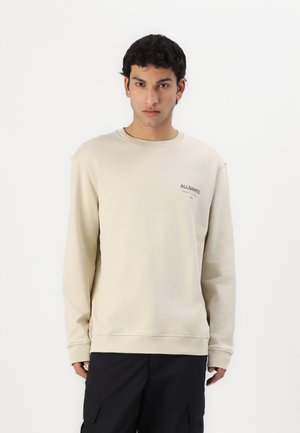 Beiger Sweatshirt mit langen Ärmeln und Rundhalsausschnitt, ausgestattet mit einem dezenten Logo auf der linken Brust. Hergestellt aus weichem, strukturiertem Stoff.