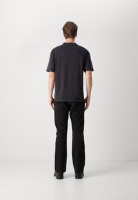 Camiseta negra de manga corta con un corte relajado, llevada con jeans negros. La parte posterior presenta un diseño simple y una textura de tela suave.