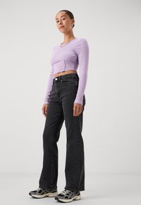 Light purple ribbed long-sleeve crop top with a round neckline, paired with high-waisted black jeans and athletic sneakers.