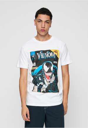 Junger Mann mit kurzen lockigen Haaren, der ein weißes T-Shirt mit einem farbenfrohen Venom-Comic-Cover-Design trägt.