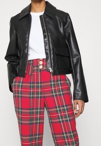 Svart konstläderjacka med dragkedja fram, stor krage och sidofickor. Tillsammans med röda rutiga höga byxor med guldknappar.