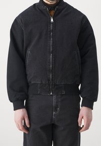 Czarna bomberka z denimu z zamkiem błyskawicznym z przodu, ściągaczami na mankietach i dole. Posiada boczne kieszenie oraz kontrastowy wzór na rękawach.