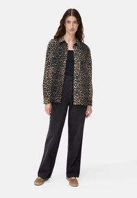 Leopard print shirt jacket in beige and black, featuring a collar, two chest pockets, paired with black wide-leg pants and beige sneakers.