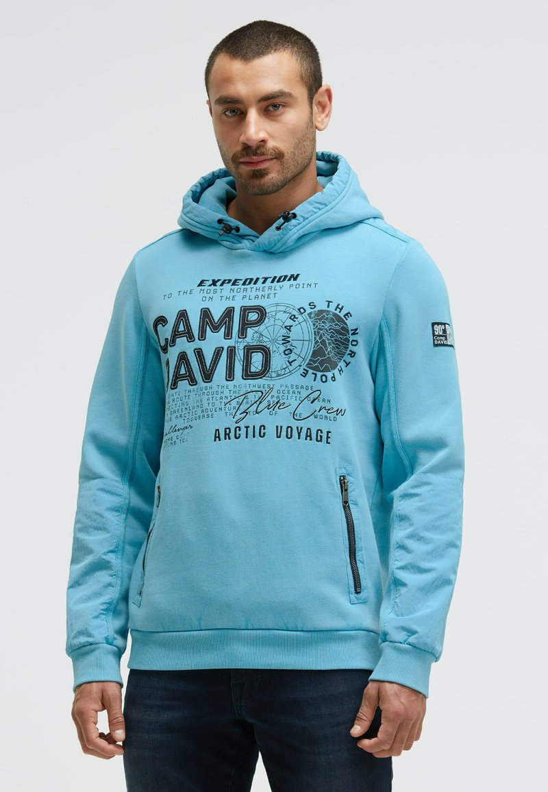 Light blue hoodie with a front graphic reading "CAMP DAVID." Features a drawstring hood, zippered side pockets, and ribbed cuffs.