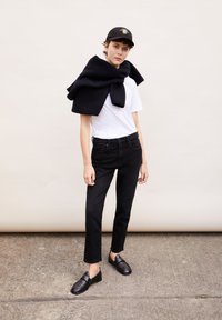 Svarta denimjeans, vit t-shirt, svart scarf draperat över axlarna och svarta slip-on skor. Kapsylen har en sol-emblem i gult.