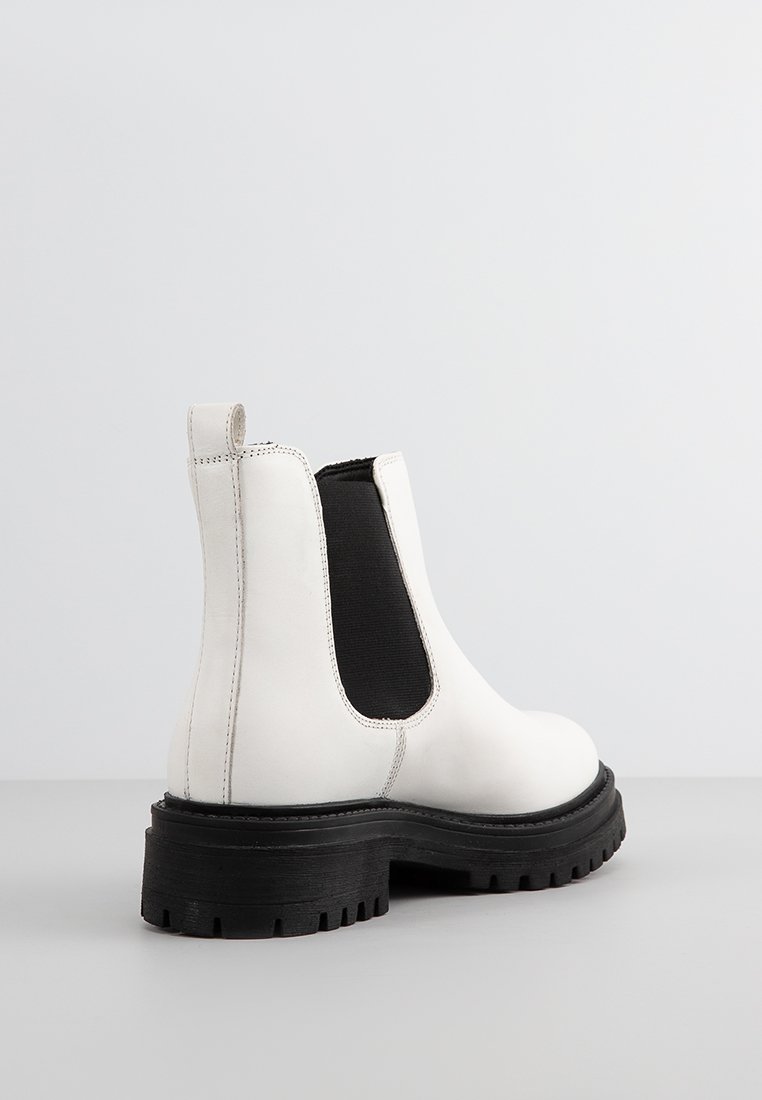 Stivaletto Chelsea in pelle bianca con pannello laterale elasticizzato nero e suola spessa nera, mostrato di profilo e da dietro su una superficie grigia.
