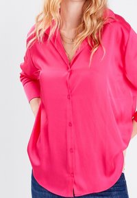 Chemise rose vif en satin, à boutons, avec une coupe décontractée, des manches longues et un ourlet légèrement arrondi. Dotée d'un col classique et de boutons sur le devant.