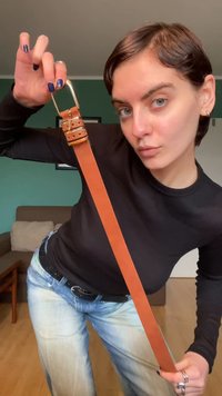 Ζώνη από δέρμα σε ταμπά απόχρωση με χρυσή μεταλλική αγκράφα, διαθέτει πολλαπλές τρύπες για ρύθμιση. Το μοντέλο παρουσιάζει τη ζώνη με ένα casual σύνολο.