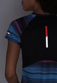 Camiseta atlética de manga corta en negro con un patrón de rayas azules, que presenta un acento reflectante y una raya vertical roja y blanca en la parte posterior.