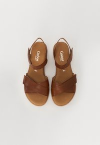 Brown leather sandals with crisscross straps, an open heel, and a cushioned insole. Designed for comfort with a flat sole.