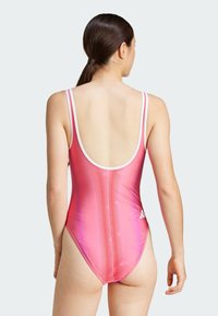 Jednodílné plavky v růžovém gradientu s bílými ramínky, s nízkým zadním dílem a texturovaným vzorem. Logo značky na levém boku.