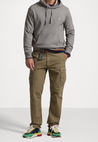 Grå huvtröja, olivgröna cargobyxor med sidofickor och färgglada sneakers med gröna, blå, röda och gula detaljer.