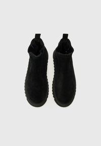 Bottines noires en daim avec une surface texturée, des panneaux latéraux élastiques, des languettes de tirage et des semelles en caoutchouc avec un bord dentelé.