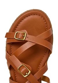 Sandalo in pelle marrone con due cinturini intrecciati con fibbie dorate sulla parte superiore e suola cucita visibile su sfondo bianco.