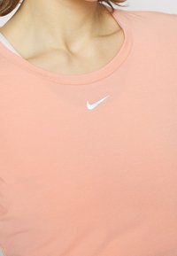 T-shirt Nike couleur pêche avec un col rond, arborant un logo Nike blanc sur la poitrine et un tissu lisse et doux.