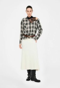 Mustvalge ruuduline särk pitsdetailiga, valge seelik, pruun vöö logoga, mustad pahkluu saapad metallist aksessuaaridega.