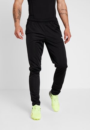 Schwarze Sport-Jogginghosen mit elastischem Bund, körpernahem Schnitt und Seitentaschen. Getragen mit leuchtend grünen Sportschuhen.