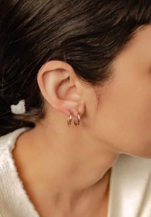 Roségoldene Creolen, die nah am Ohrläppchen sitzen, mit einem glatten, runden Design, glänzenden Texturen und einem minimalistischen Stil.