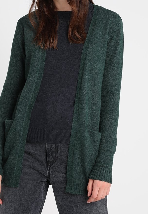 Green knit cardigan with a loose fit, open front, and ribbed cuffs. Features two front pockets and a soft texture. Worn over a dark sweater.