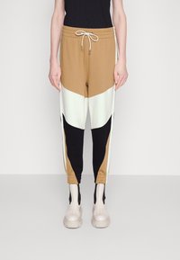 Color-blocked joggers featuring brown, cream, and black panels; elastic waistband with drawstring; tapered cuffs; soft, stretchy material.