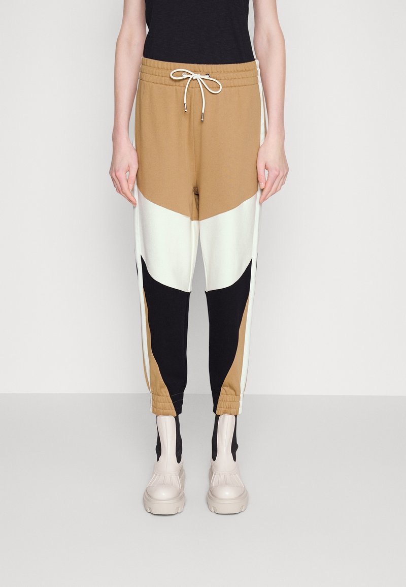 Color-blocked joggers featuring brown, cream, and black panels; elastic waistband with drawstring; tapered cuffs; soft, stretchy material.