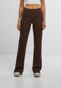 Pantalons en tricot côtelé marron avec une silhouette évasée et une taille élastique, présentant une texture douce et un design décontracté.