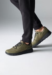 Zelené sportovní boty s texturovaným textilním svrškem, černými šňůrkami a gumovou podrážkou. Nabízí polstrovaný design a akcenty s dírkami.