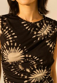 Zwarte mouwloze jurk met een gerimpeld ontwerp, versierd met een wit tie-dye patroon dat op zonnestralen lijkt, gemaakt van zachte stof.
