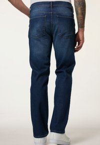 Vaqueros de mezclilla en azul oscuro con un corte recto, que presentan dos bolsillos traseros y detalles de costura sutiles, combinados con zapatillas blancas.