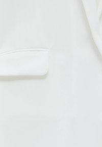 Tejido de blazer blanco con una textura suave y mate. Presenta una forma ajustada y un bolsillo de ojal en el lado izquierdo delantero.