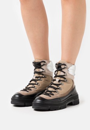 Beige, black, and white lace-up ankle boots with chunky soles worn on bare legs against a plain white background.
