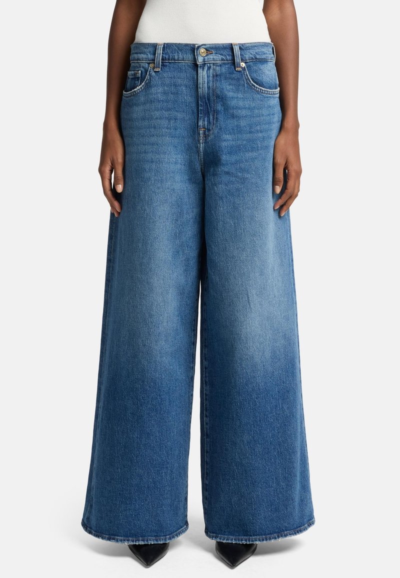 Ljusa blå vida jeans i denim, med hög midja, framfickor och fransad nederkant, kombinerat med spetsiga svarta skor.