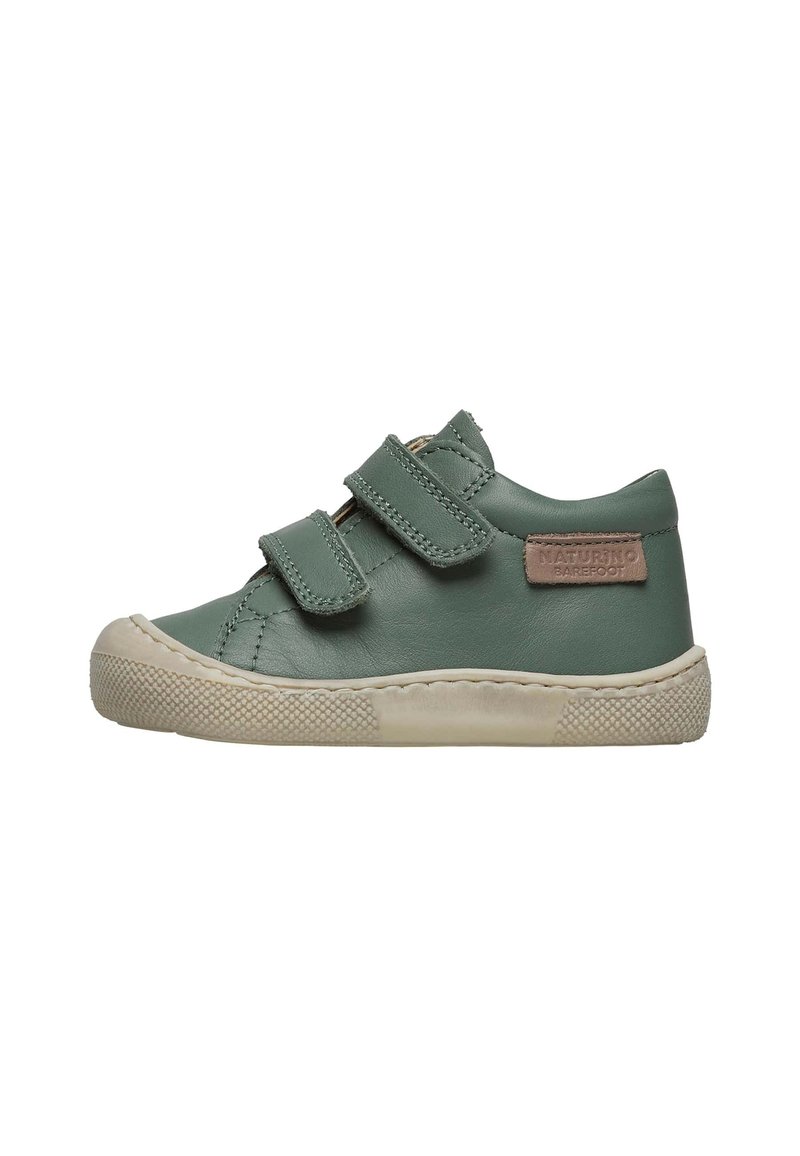 Zapato de cuero verde con dos correas de Velcro, suela de goma crema, puntera texturizada y un parche de marca en el lado exterior.