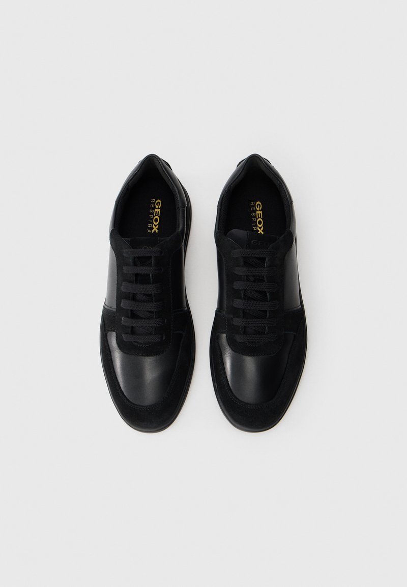 Zapatillas negras que combinan materiales de cuero y ante, con puntera redonda, cordones y un branding sutil en la plantilla y el lateral.
