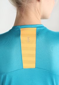 Tyrkysové sportovní tričko s texturovanou žlutou panelem na zádech, s horizontálními pruhy a logem umístěným nahoře.