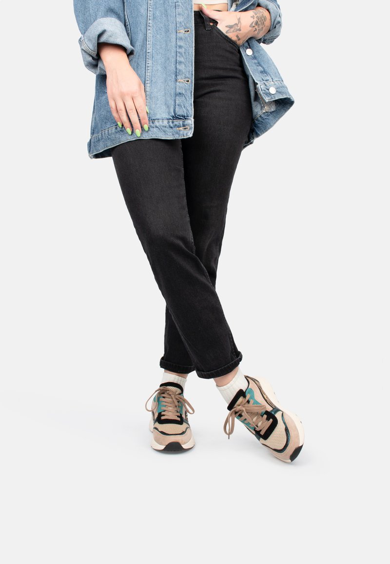 Jeans noirs taille haute associés à une veste en denim clair et des baskets beiges avec des accents bleu sarcelle et des semelles noires, accompagnées de chaussettes blanches.