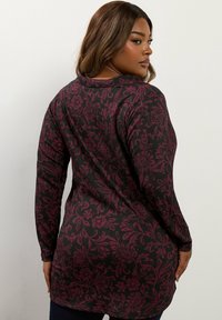 Czarna tunika z długim rękawem z ciemnoczerwonym florystycznym wzorem, teksturowana tkanina, zaokrąglony dół i luźny krój. Pokazany widok z tyłu.