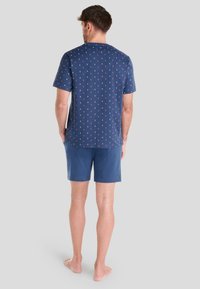 Camisa de manga corta azul marino con un patrón de anclas rojas y blancas, combinada con pantalones cortos azules a juego. Material de algodón, ajuste casual.