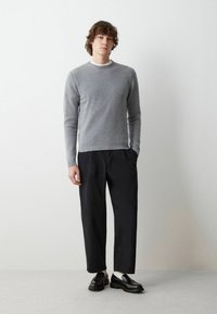 Maglione grigio a maglia con orlo a coste, pantaloni neri con tasche e mocassini neri. Design semplice e moderno con colori neutri.