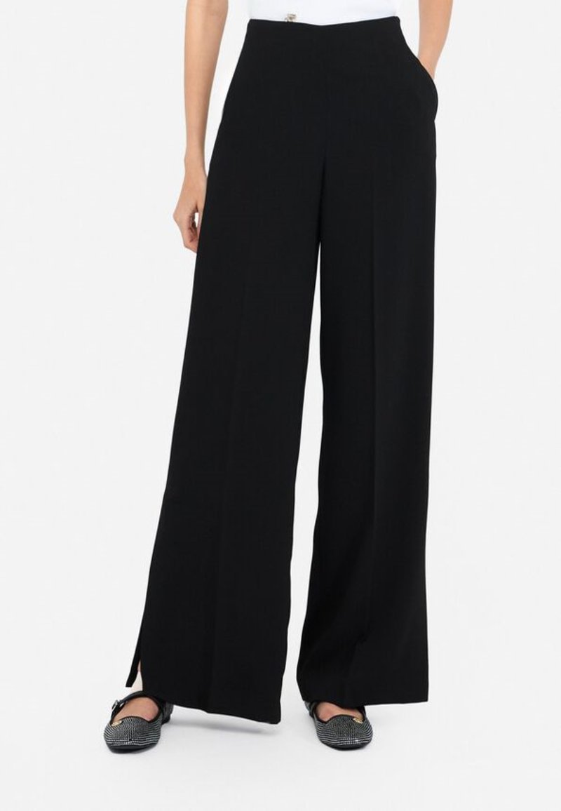 Pantalones de pierna ancha negros con una textura suave, pliegues frontales y bolsillos laterales. Presenta un diseño elegante y minimalista con una sutil abertura frontal.