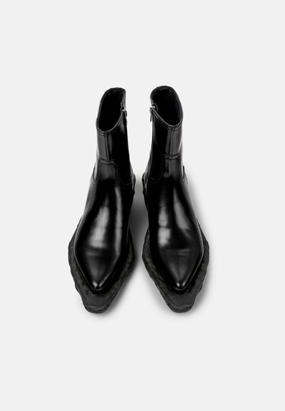 Botas de tobillo de cuero negro con punta afilada, que cuentan con una suela gruesa texturizada y cierre de cremallera en la parte trasera. Superficie lisa con acentos mínimos.