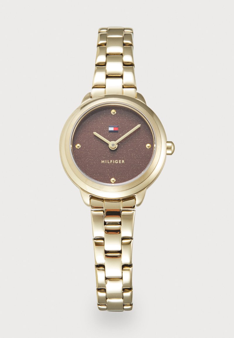 Montre en métal doré avec un boîtier rond et un cadran brun texturé. Dispose de trois aiguilles dorées et de petits repères horaires dorés. Bracelet de style bande.