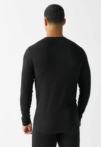 Maglietta nera a maniche lunghe realizzata in tessuto leggero, con un design aderente e scollo rotondo. Texture liscia senza motivi visibili.