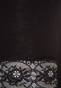 Tela negra con una textura suave presenta un detalle de encaje en la parte inferior, adornada con patrones florales y bordes festoneados.