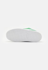 Grønne mokasiner i semsket lær med en hvit gummibunn som har et teksturert mønster for grep. Minimalistisk design uten synlig merking.
