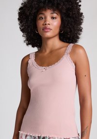 Débardeur côtelé rose clair avec une dentelle le long de l'encolure et des bretelles, présentant un petit détail de nœud au centre avant. Tissu texturé.